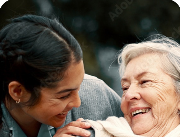 A caregiver resting her hands on the shoulders of a laughing older woman