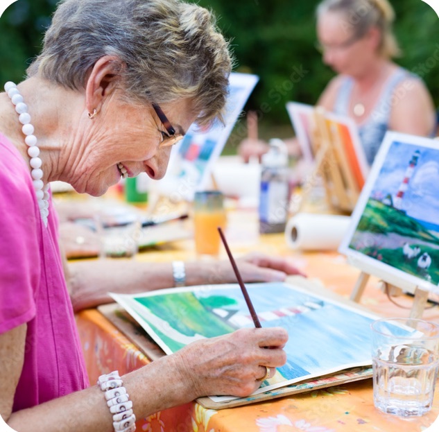 A smiling woman painting a watercolor at an outdoor art class